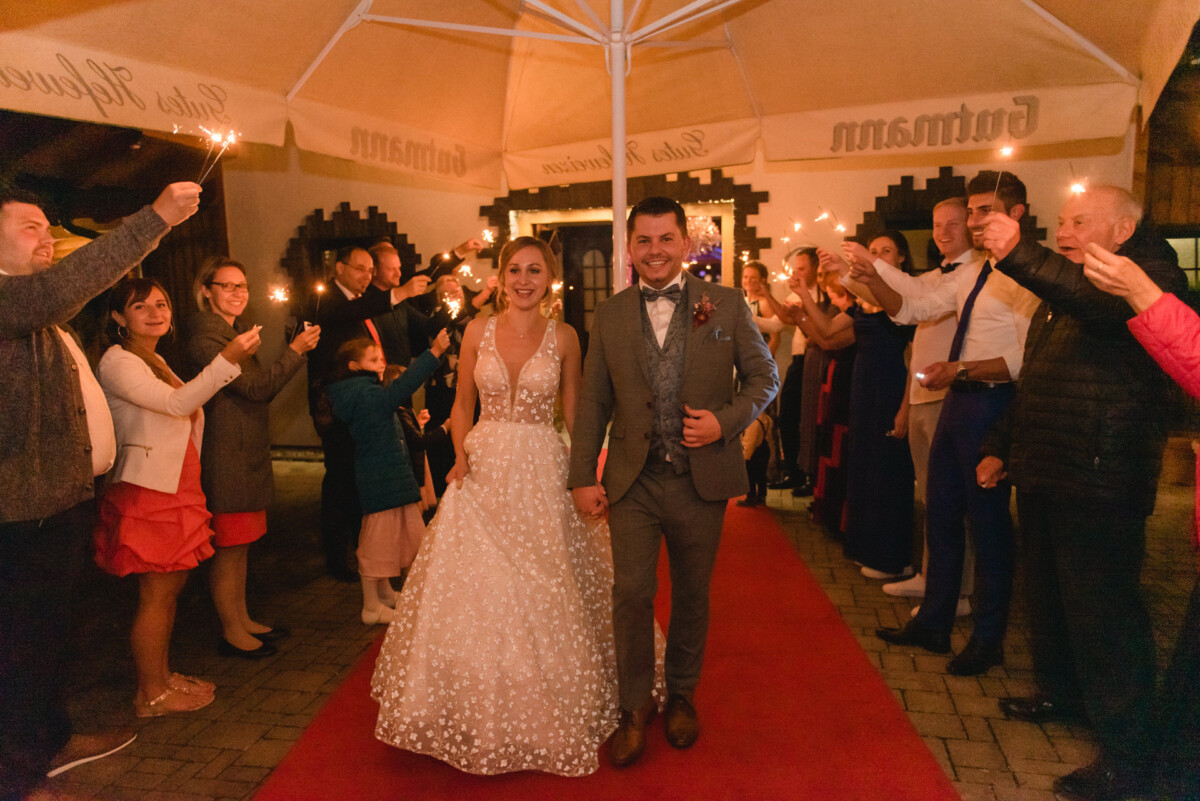 Eine Braut und ein Bräutigam, die mit Wunderkerzen in ihren Händen einen roten Teppich hinuntergehen im Land-Steakhaus Bürger in Marxheim