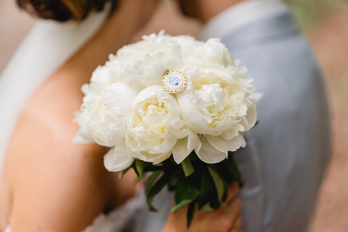 Eine Braut hält einen Strauß weißer Blumen mit einer kleinen dekorativen Uhr als Anstecknadel.