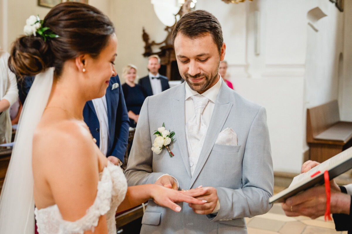 Braut und Bräutigam tauschen während ihrer Hochzeitszeremonie in einer Kirche, umgeben von Gästen, Ringe aus.