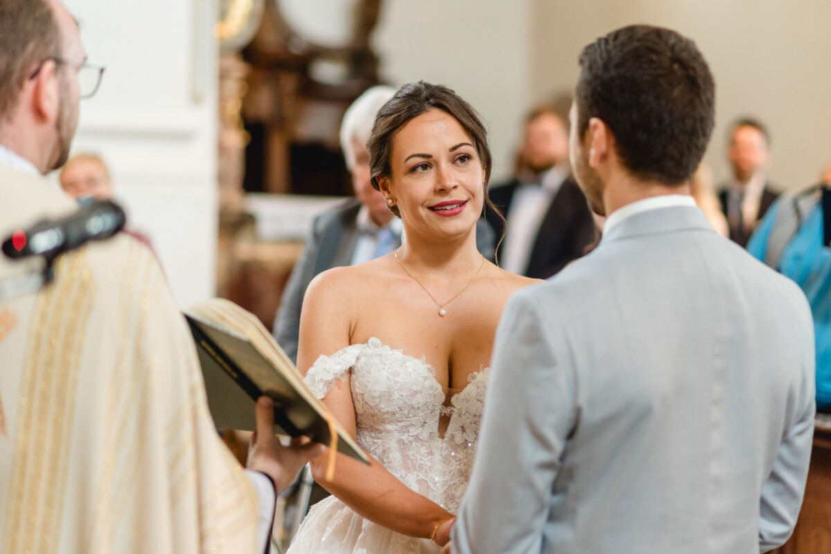 Braut und Bräutigam stehen sich während der Hochzeitszeremonie gegenüber. In der Nähe hält ein Geistlicher ein offenes Buch.
