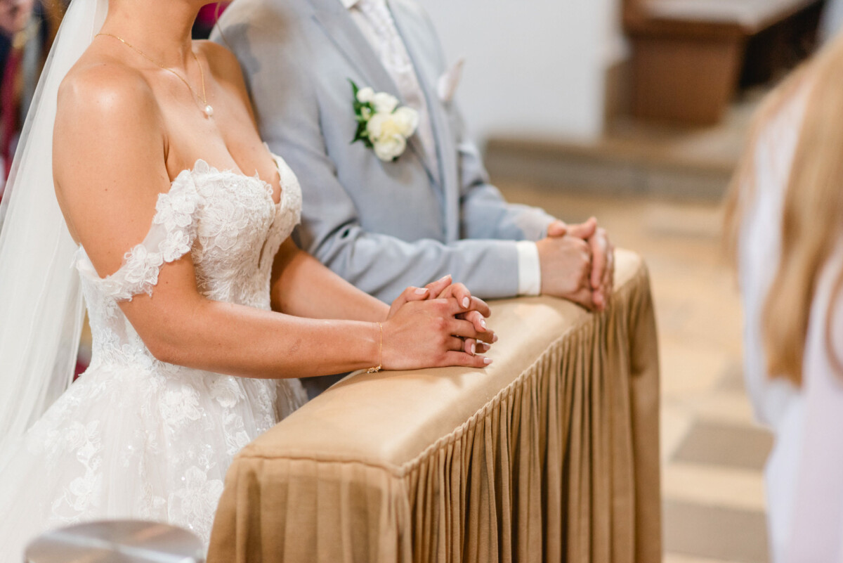 Braut und Bräutigam stehen Seite an Seite vor einem Altar und haben die Hände ineinander verschränkt.