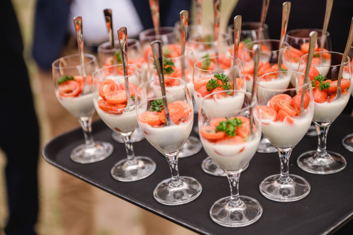 Gläser gefüllt mit einem cremigen Dessert, garniert mit geschnittenen Kirschtomaten und Petersilie, serviert auf einem schwarzen Tablett mit Löffeln.