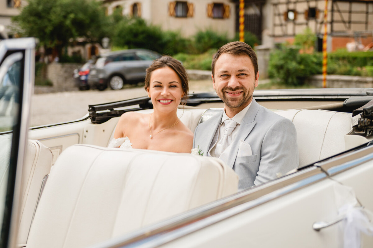 Ein Paar im Hochzeitskleid sitzt in einem weißen Cabrio.