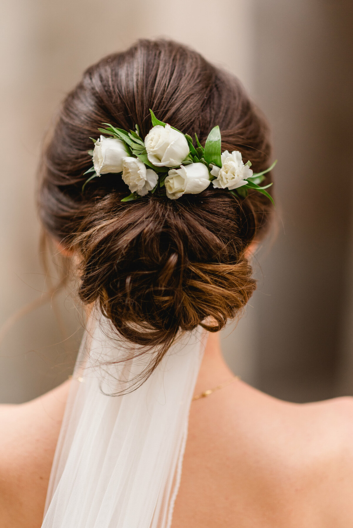 Eine Frau mit hochgestecktem braunem Haar, geschmückt mit weißen Rosen, trägt einen weißen Schleier.