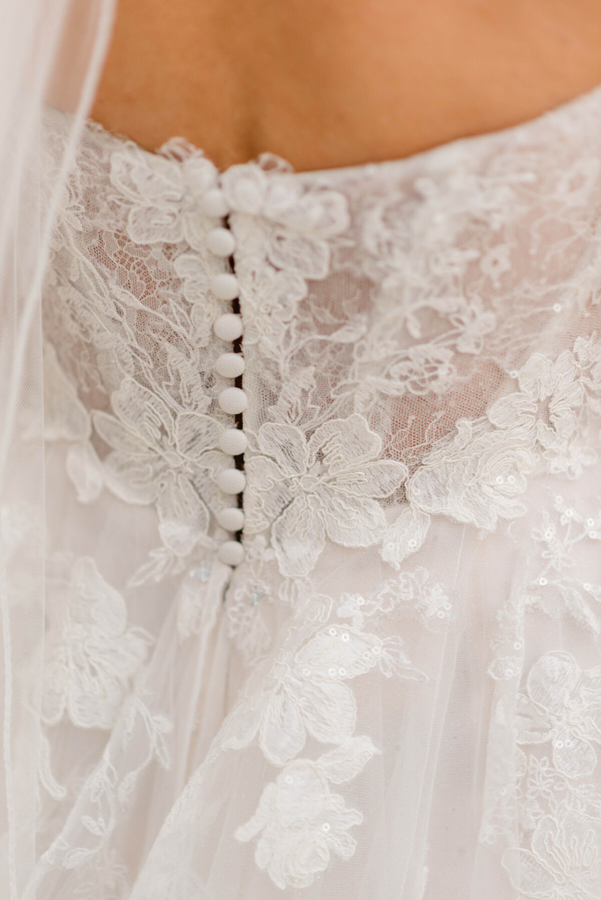 Nahaufnahme der Rückseite eines Spitzenbrautkleides mit Blumenstickerei und stoffbezogenen Knöpfen.
