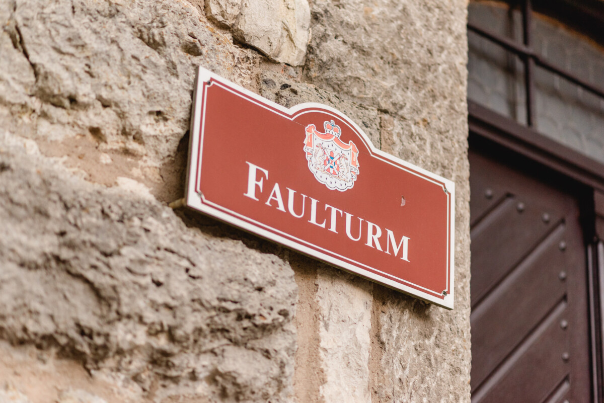 Ein rotes Schild mit weißer Aufschrift „Faulturm“ ist an einer strukturierten Steinmauer angebracht.