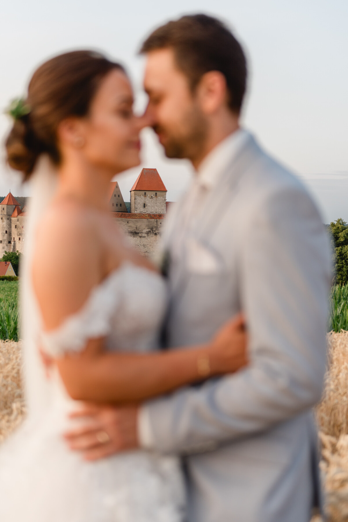 Braut und Bräutigam im Hochzeitskleid umarmen sich und verschwimmen leicht, während sie in der Nähe eines alten Schlosses im Hintergrund stehen.