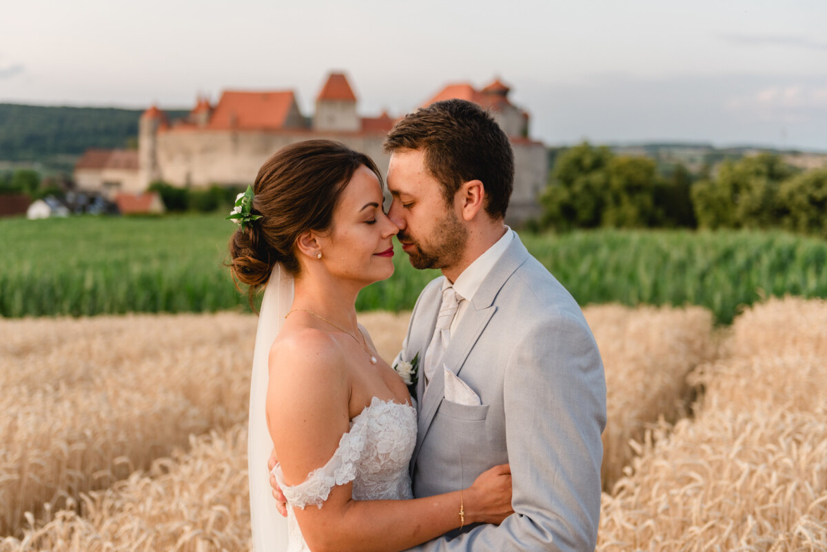 Braut und Bräutigam umarmen sich in einem Weizenfeld, im Hintergrund ist ein Schloss zu sehen.