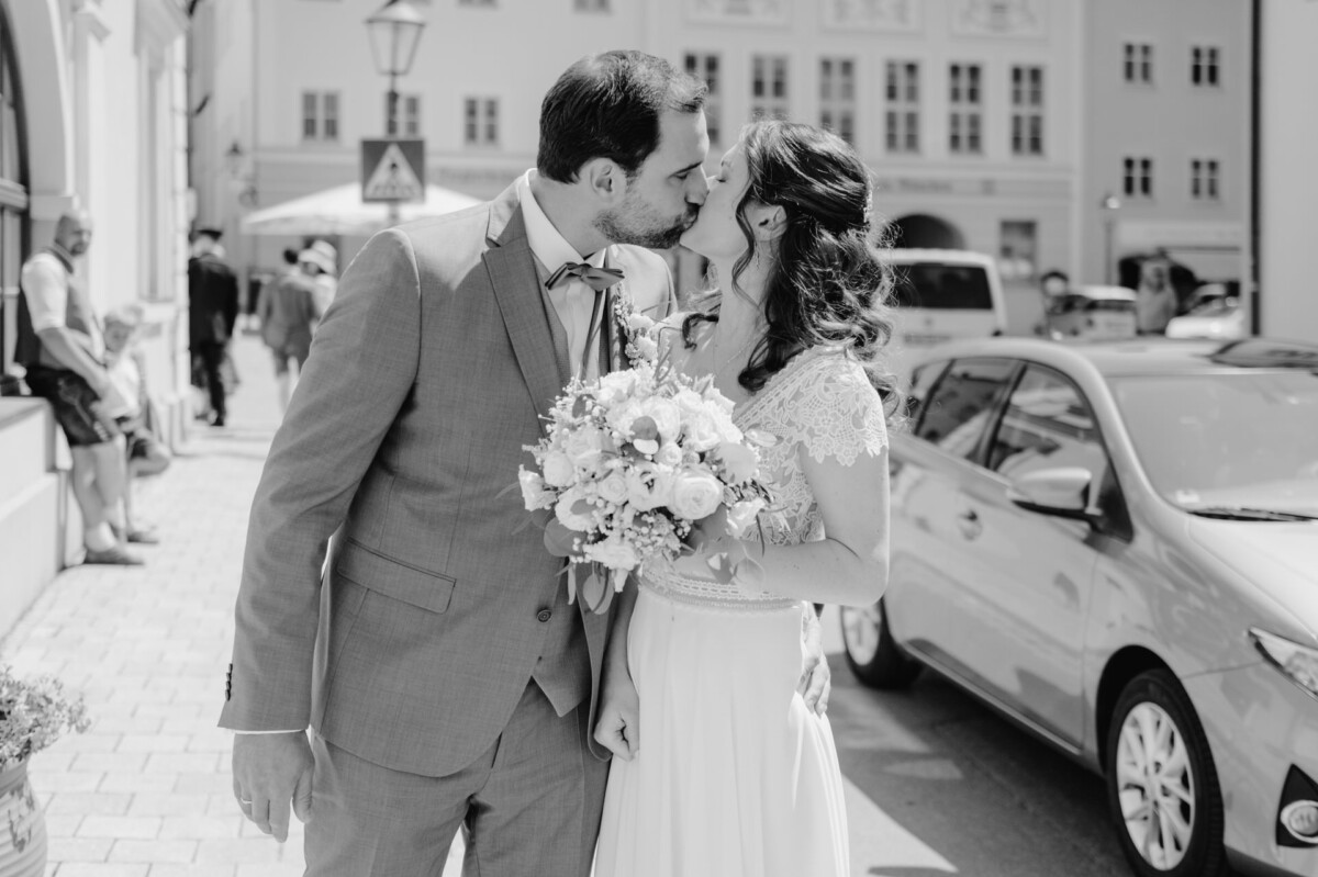 Ein Brautpaar küsst sich vor einem Auto.