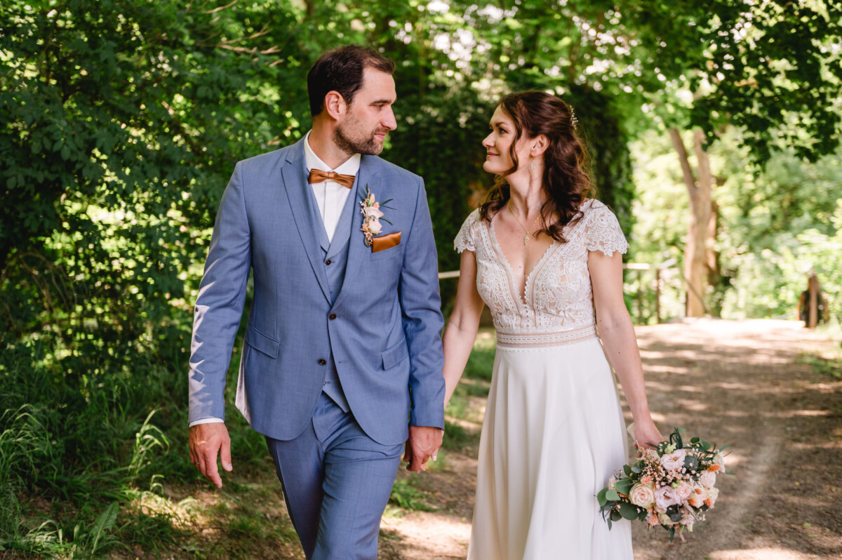 Eine Braut und ein Bräutigam gehen einen Pfad im Wald entlang.