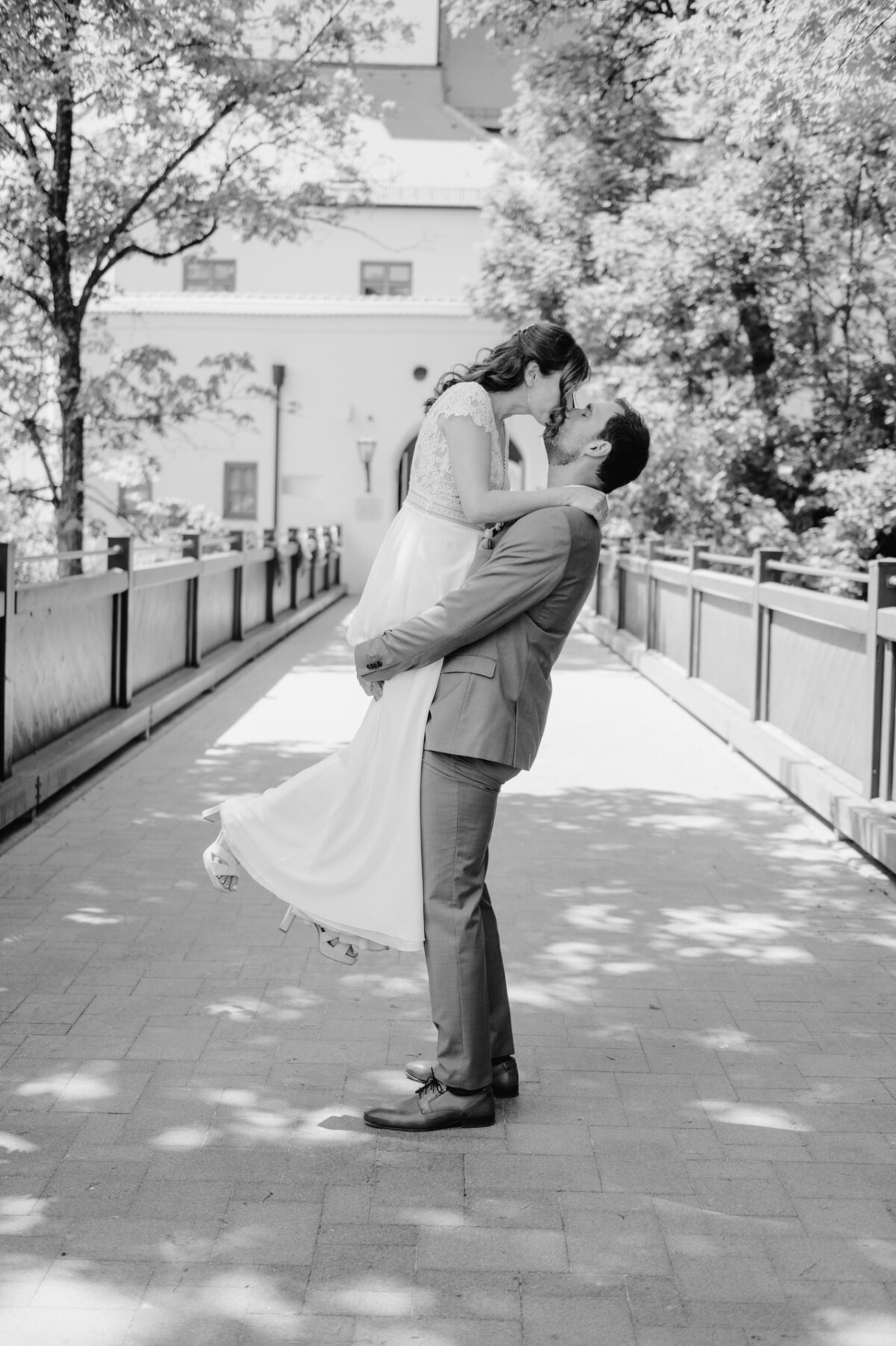 Schwarz-Weiß-Foto einer Braut und eines Bräutigams, die sich auf einer Brücke umarmen.