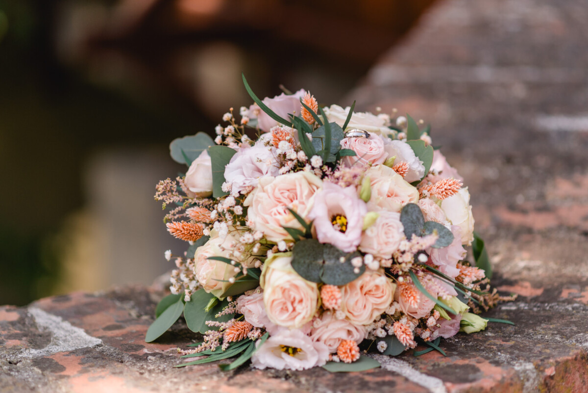 Ein Strauß rosa und pfirsichfarbener Blumen steht auf einer Ziegelwand.