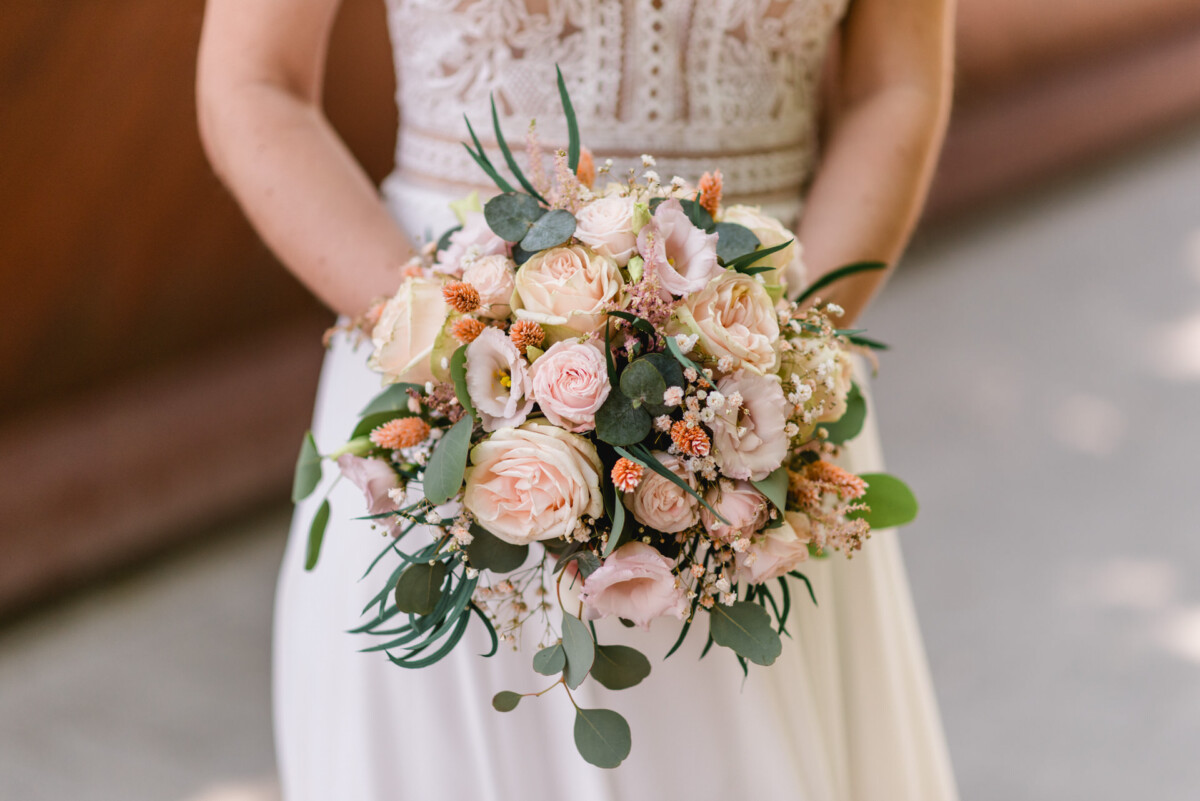 Eine Braut in einem weißen Kleid hält einen rosa und pfirsichfarbenen Hochzeitsstrauß.