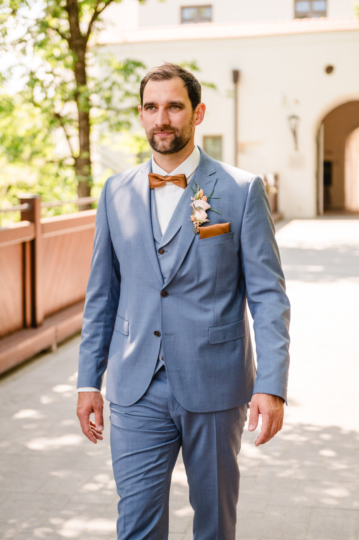 Ein Bräutigam im blauen Anzug geht einen Weg entlang.
