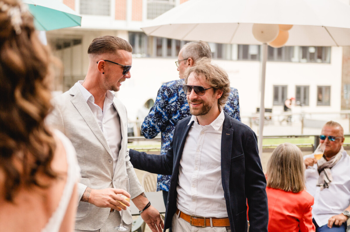 Zwei Männer reden bei einer Hochzeit im Freien miteinander.