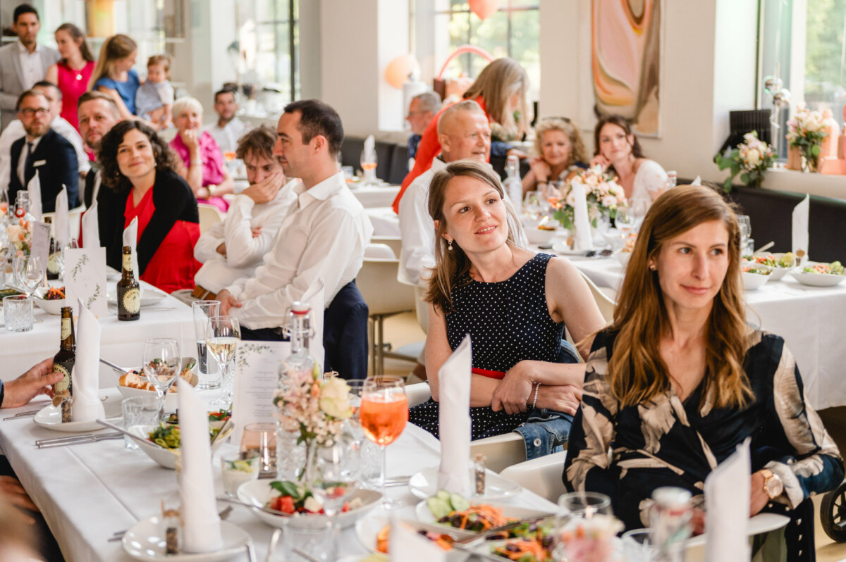 Eine Gruppe von Menschen sitzt bei einer Hochzeitsfeier an Tischen.