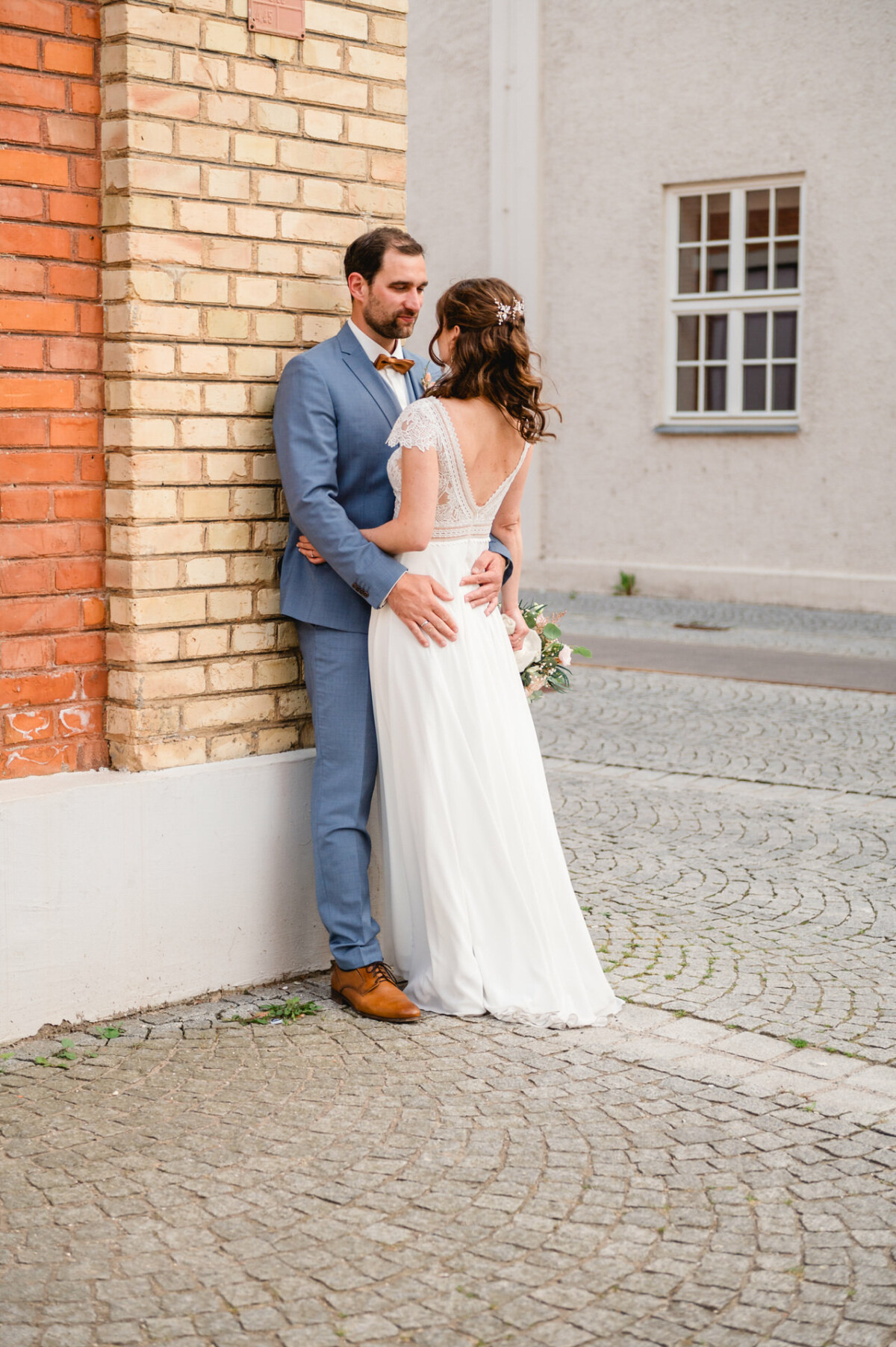 Eine Braut und ein Bräutigam umarmen sich vor einem Backsteingebäude.