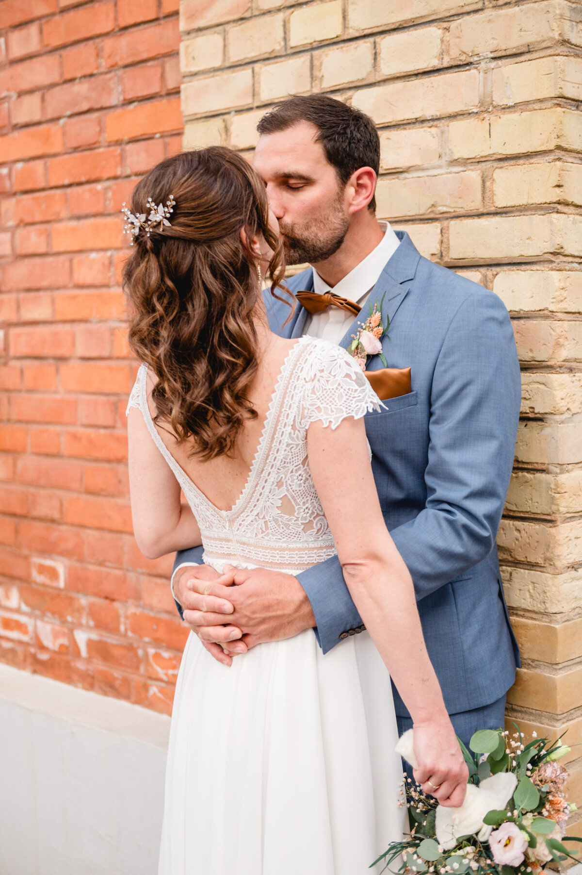 Ein Brautpaar küsst sich vor einer Ziegelwand.