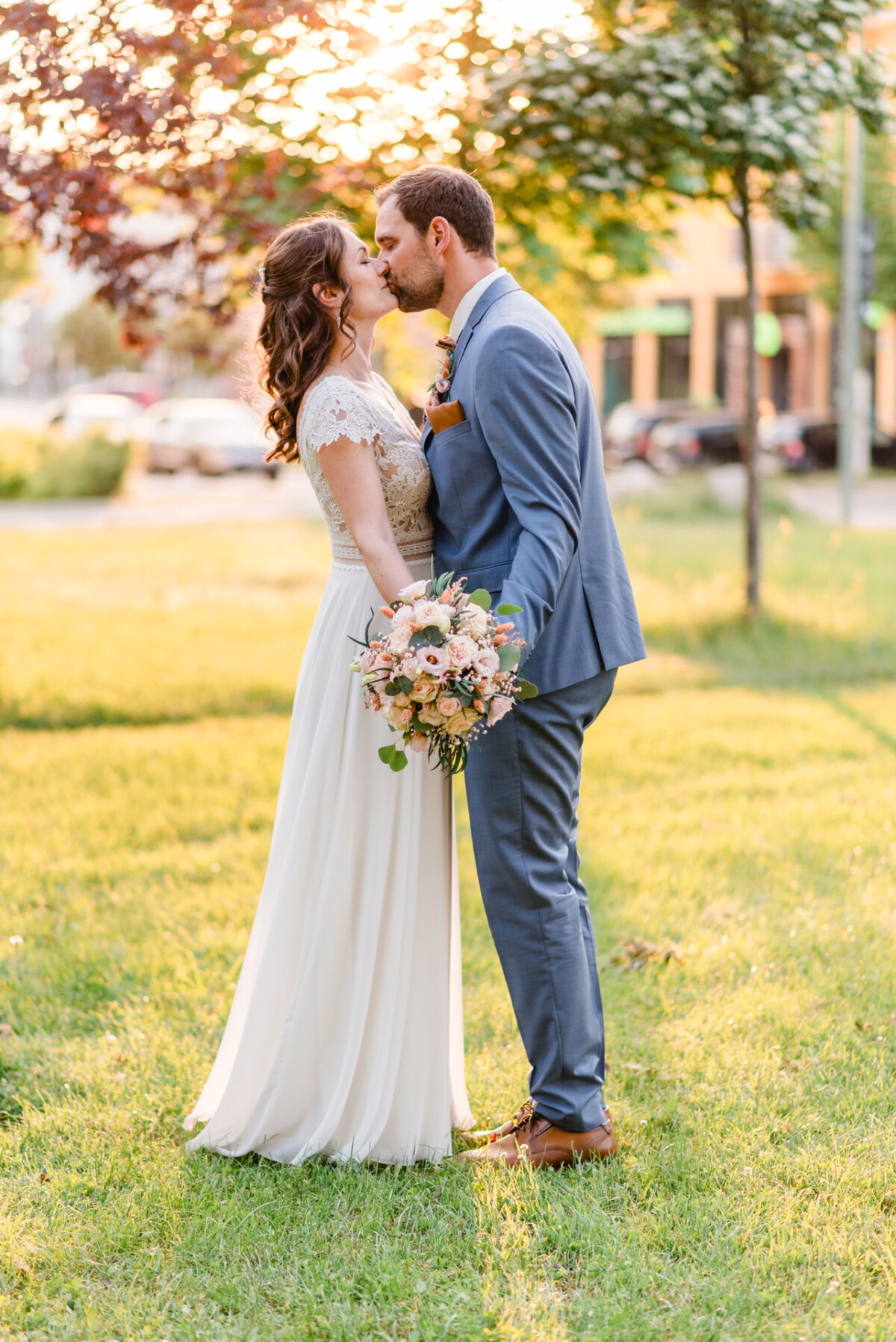 Eine Braut und ein Bräutigam küssen sich bei Sonnenuntergang im Gras.