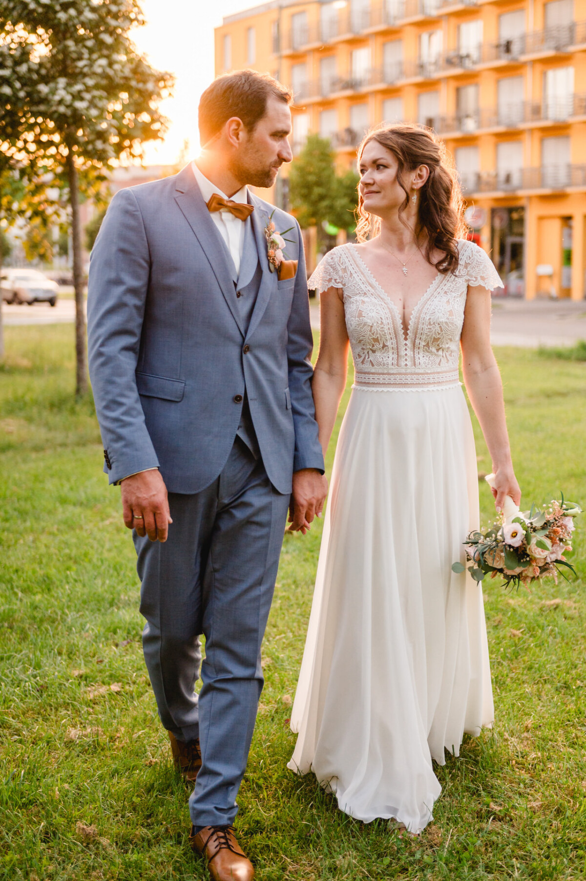 Eine Braut und ein Bräutigam gehen bei Sonnenuntergang im Gras spazieren.