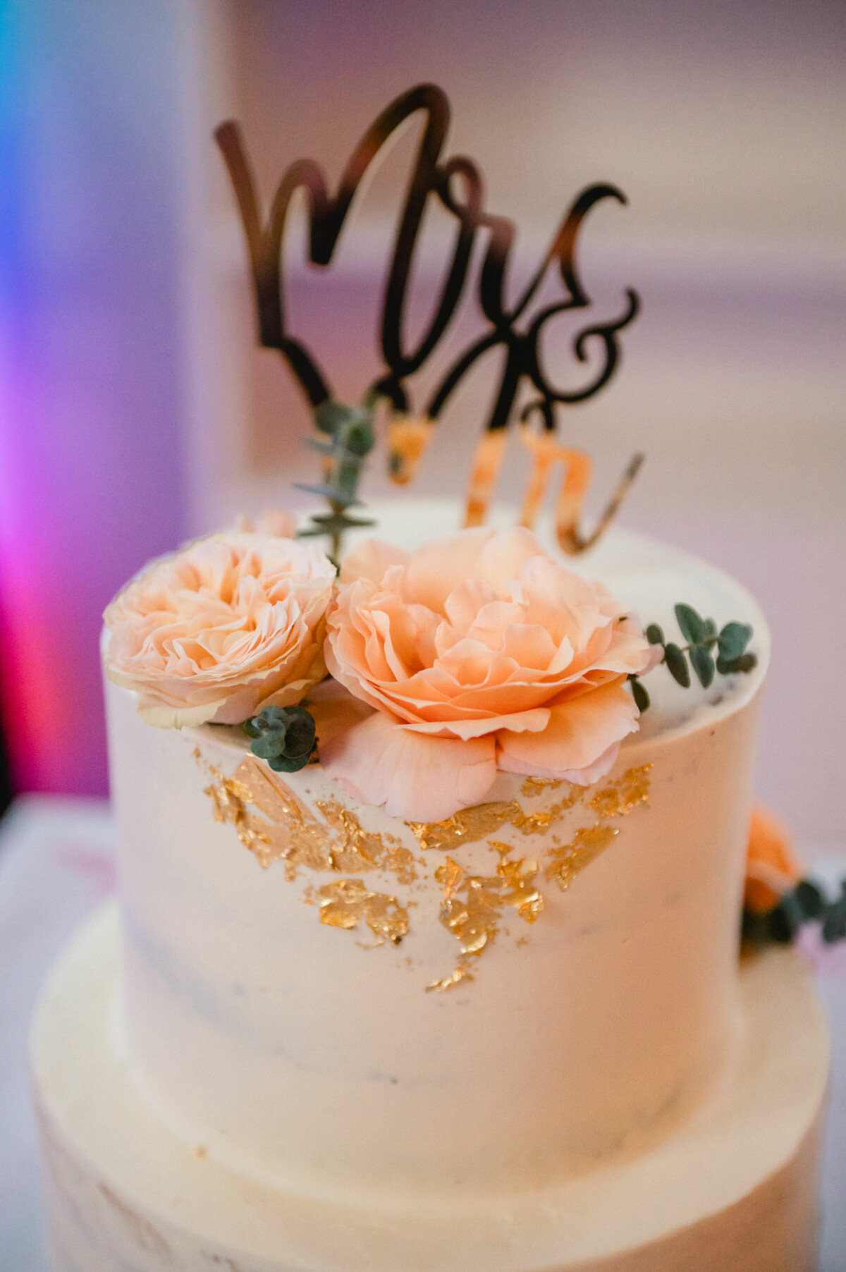 Eine Hochzeitstorte, dekoriert mit Pfirsichblüten und goldenem Schriftzug.
