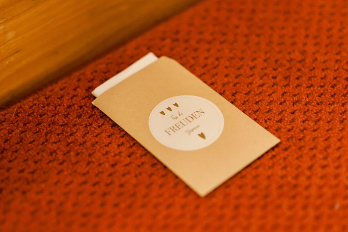 christian-lorenz.net Auf einer orange strukturierten Oberfläche liegt ein braunes Papierpäckchen mit der Aufschrift „Für die FREUDEN-Tränen“.
