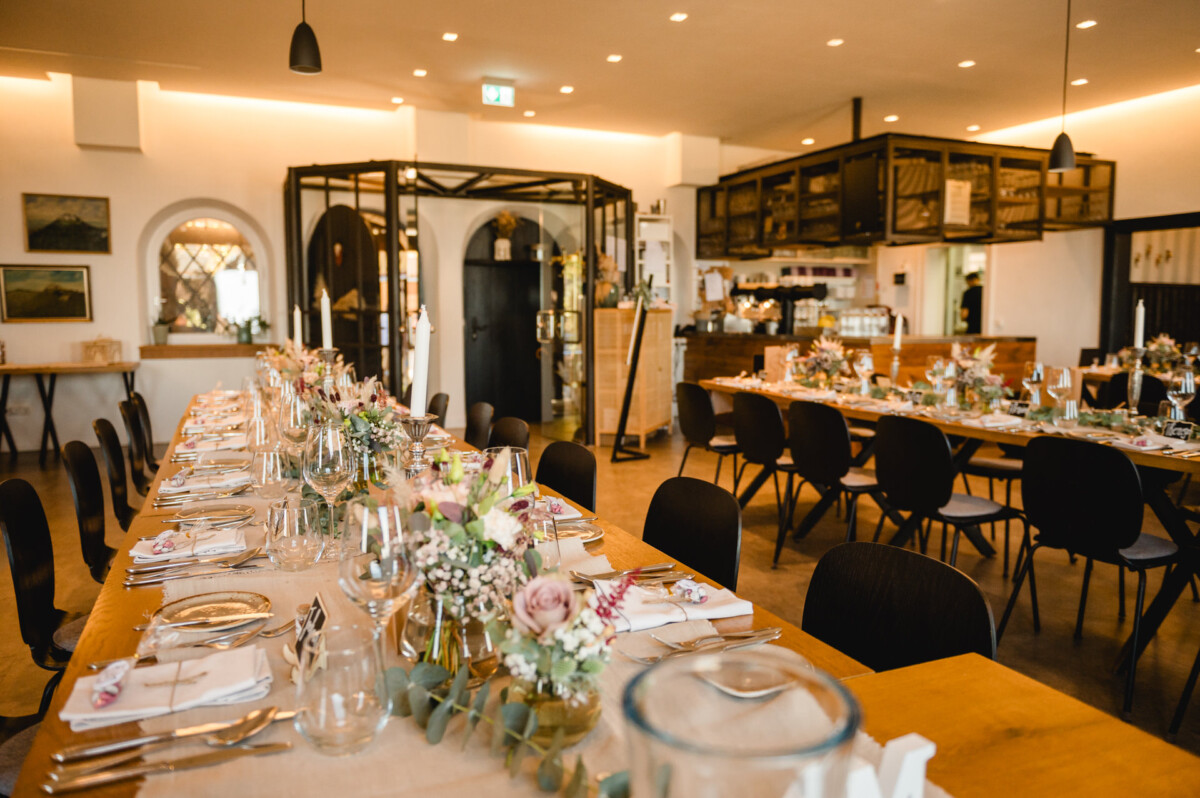 Ein wunderschön gedeckter, langer Esstisch mit floralen Tischdekorationen im Interieur eines eleganten Restaurants, bereit für eine formelle Veranstaltung.