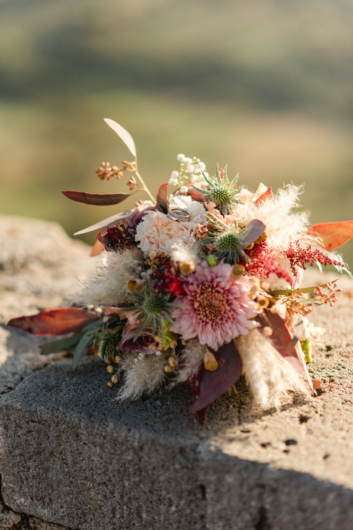 christian-lorenz.net Ein Strauß mit rosa und weißen Blumen, braunen Blättern und Grünpflanzen auf einer Steinoberfläche unter natürlichem Licht.