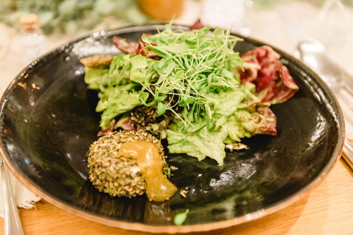 christian-lorenz.net Ein schwarzer Teller mit gemischtem Blattgemüse und Microgreens, dazu eine Käsekugel mit Kräuterkruste und einem Klecks Senfsauce.