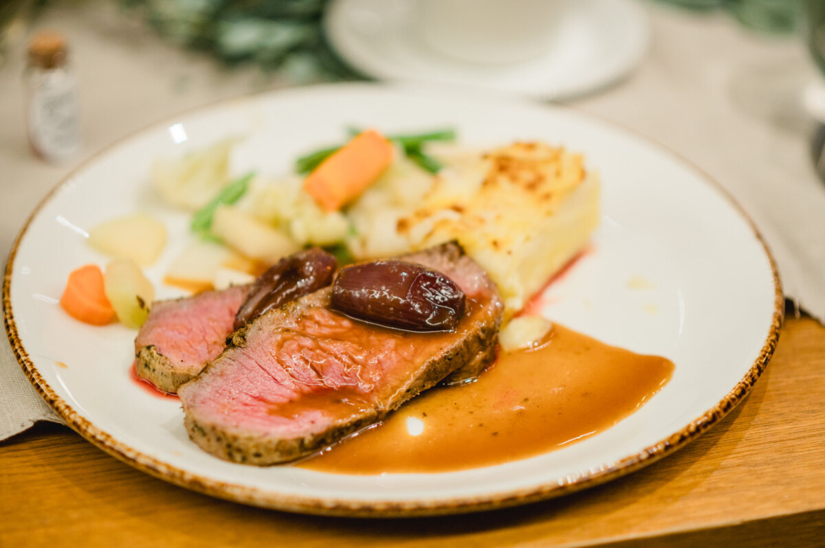 Teller mit Rindfleischscheiben in brauner Soße, garniert mit Wurzelgemüse, einer Portion Dauphinoise-Kartoffeln und einer kleinen Portion Gemüse.