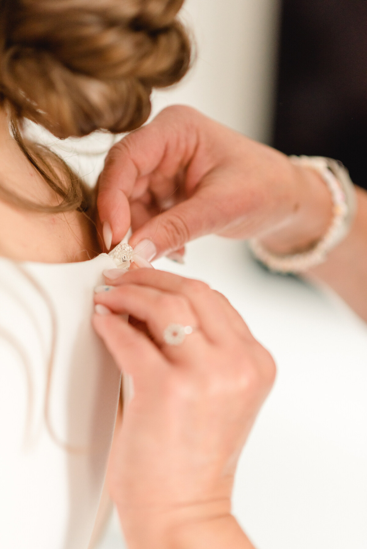 Nahaufnahme der Hände einer Frau, die einen Vintage-Perlenknopf auf der Rückseite des eleganten weißen Kleides einer anderen Frau schließen.