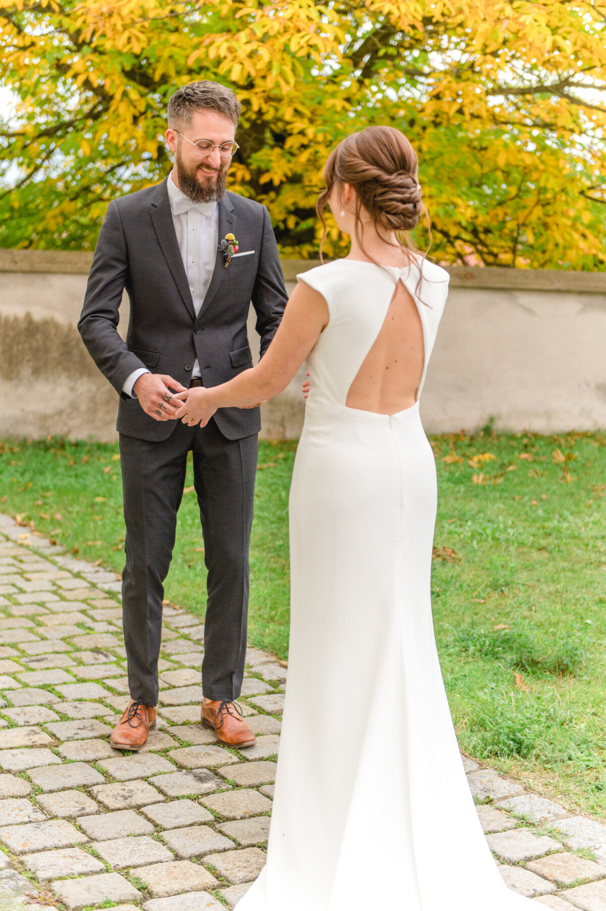 Braut und Bräutigam verbringen einen freudigen Moment auf einem Kopfsteinpflasterweg, umgeben von Bäumen mit gelbem Herbstlaub.