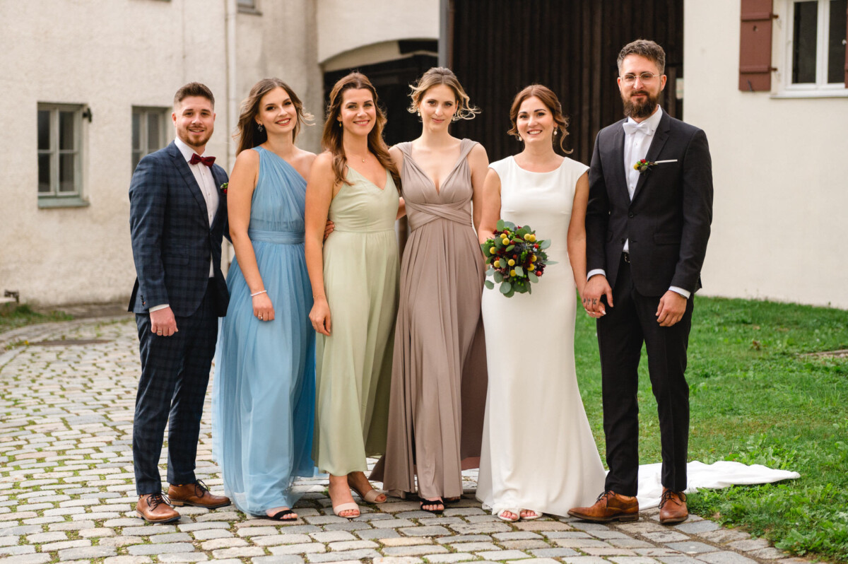 Eine Gruppe von drei Frauen und drei Männern in Abendgarderobe steht im Freien, vermutlich bei einer Hochzeit.