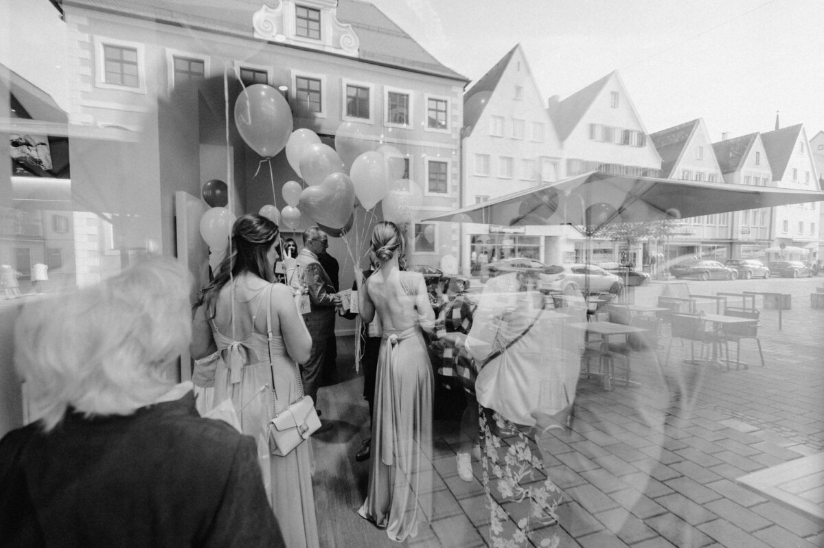 Schwarzweißfoto von Menschen mit Luftballons auf einer Stadtstraße. Das Foto zeigt Bewegungsunschärfe und Reflexionen und erzeugt so eine verträumte Atmosphäre.