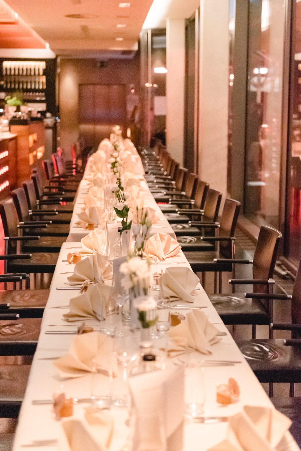 Eleganter Banketttisch mit frischer weißer Tischwäsche, feinem Porzellan und gefalteten Servietten, gesäumt von schwarzen Stühlen in einem warm beleuchteten Speisezimmer.