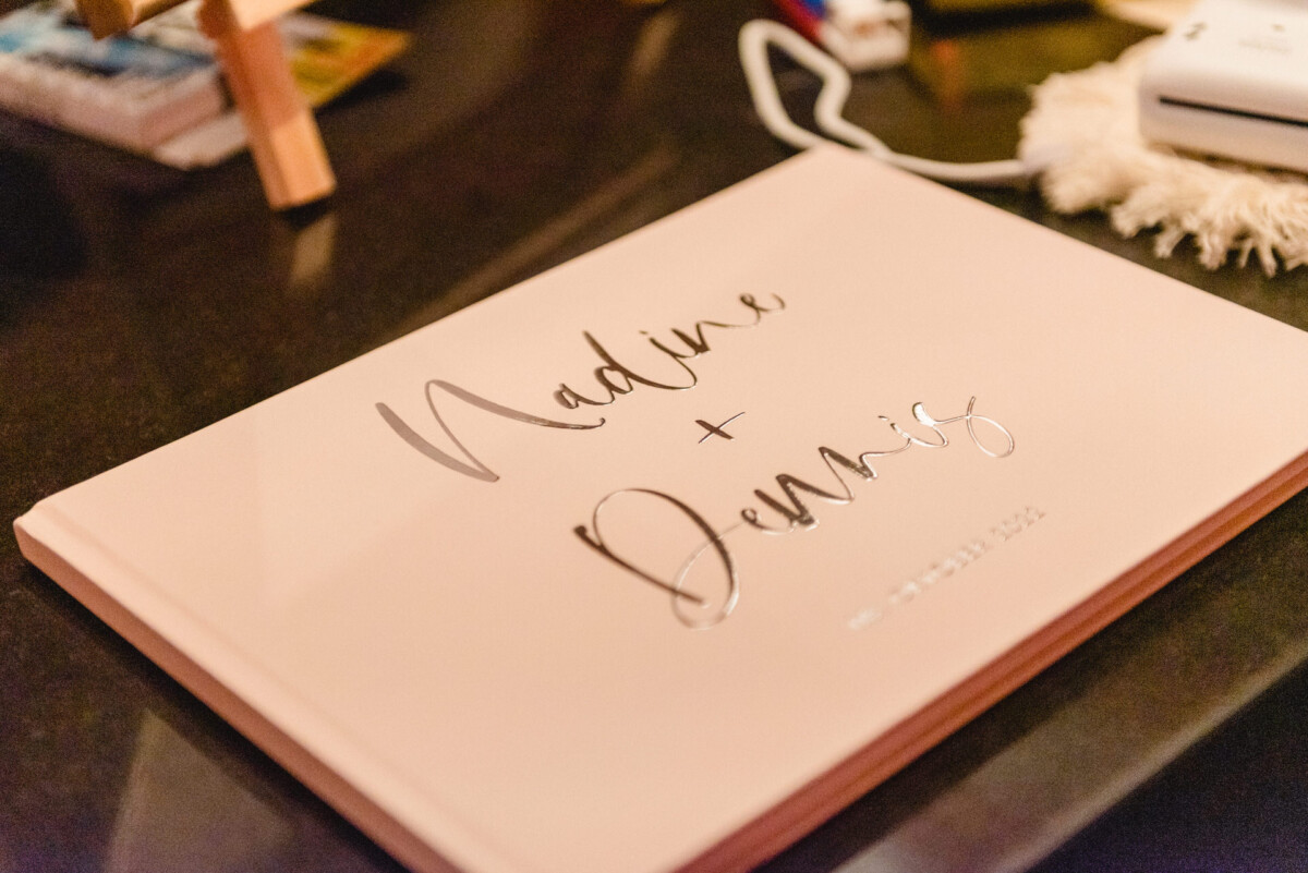 Ein Hochzeitsgästebuch auf einem Tisch mit der Handschrift „Nadine + Dennis“ und darunter dem Datum „20. Juni 2022“.