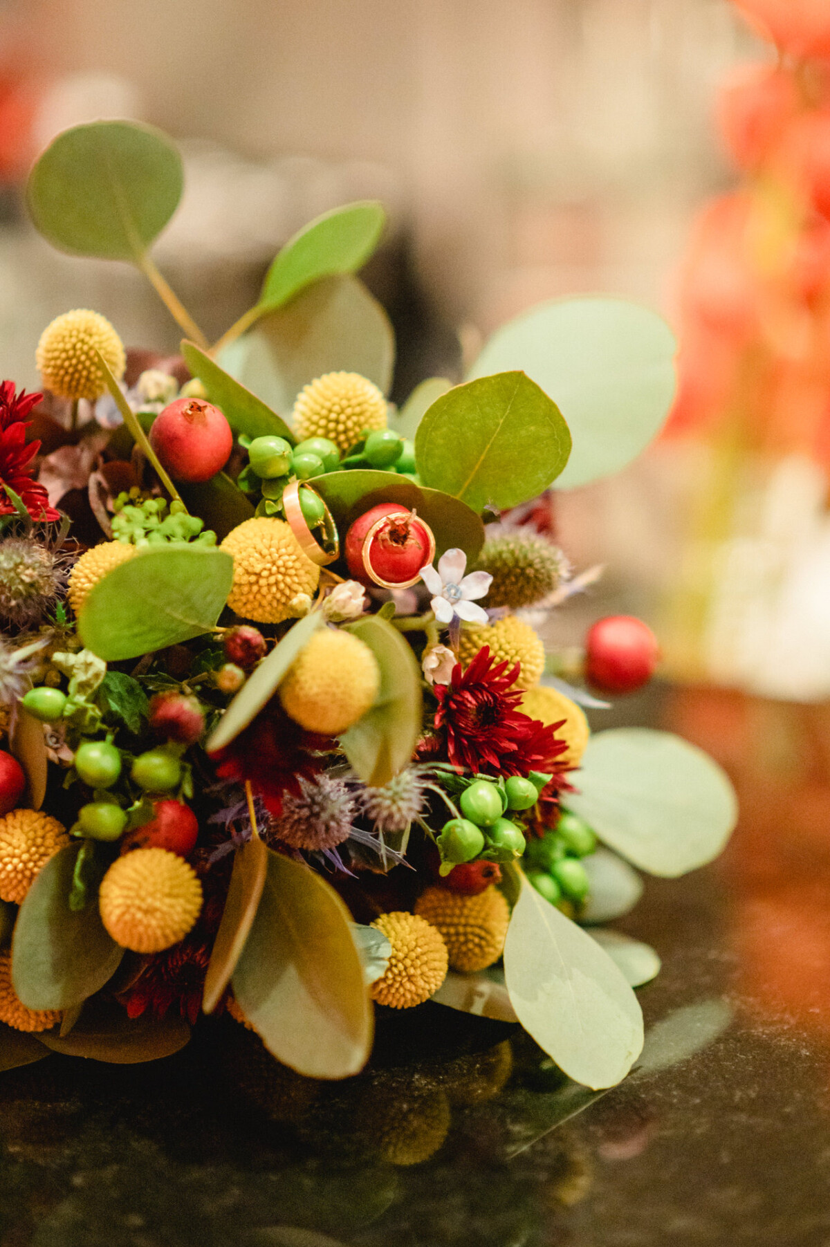 Nahaufnahme eines farbenfrohen Hochzeitsstraußes mit roten und gelben Blüten, Beeren und grünem Laub auf einer dunklen Oberfläche.