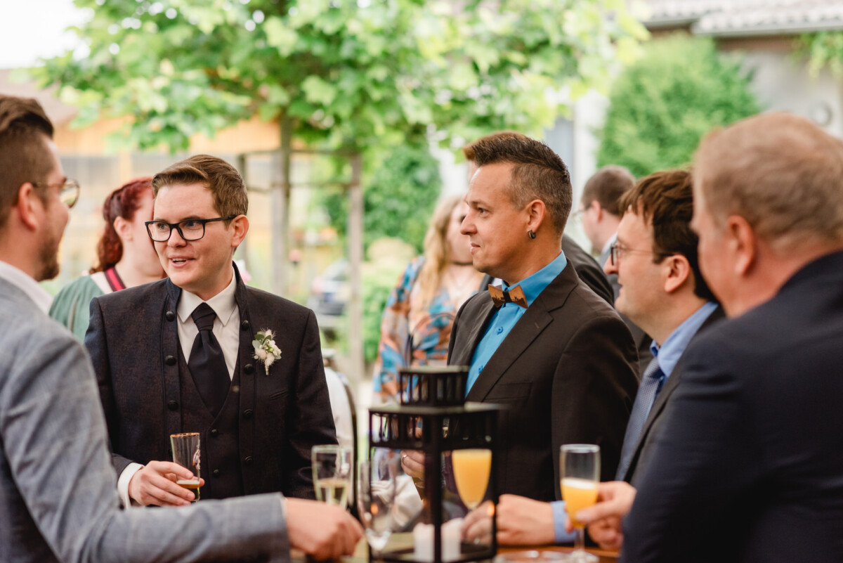 Eine Gruppe von Männern in Anzügen, einige mit Gläsern in der Hand, unterhält sich auf dem Hochzeit Schammenhof bei Langenau, Ulm. Bäume und andere Gäste bilden eine charmante Kulisse für dieses elegante Treffen im Freien. Eine Gruppe von Männern in Anzügen, einige mit Gläsern in der Hand, unterhält sich auf dem Hochzeit Schammenhof bei Langenau, Ulm. Bäume und andere Gäste bilden eine charmante Kulisse für dieses elegante Treffen im Freien.
