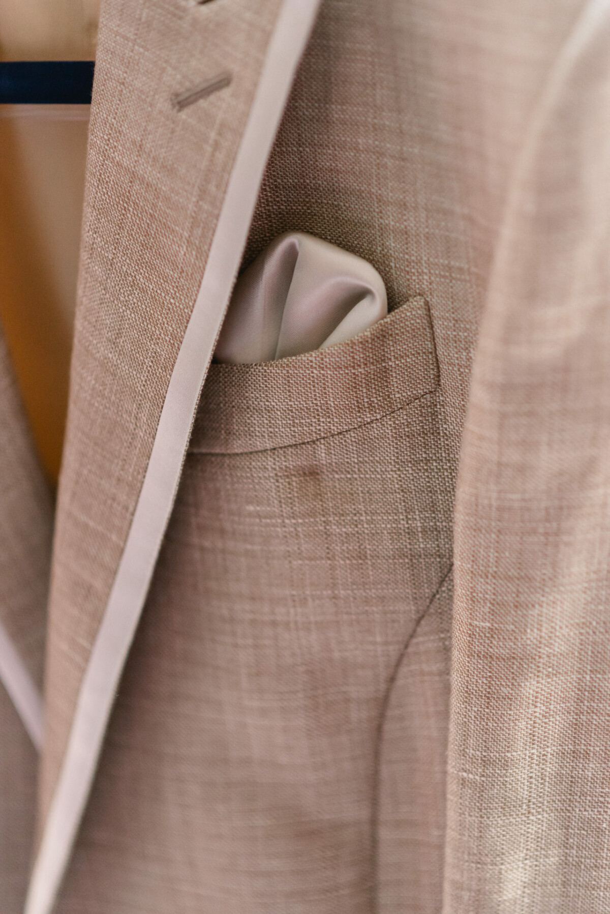 Nahaufnahme eines beigen Anzugsakkos mit einem hellen Einstecktuch, das ordentlich in die Brusttasche gesteckt ist.