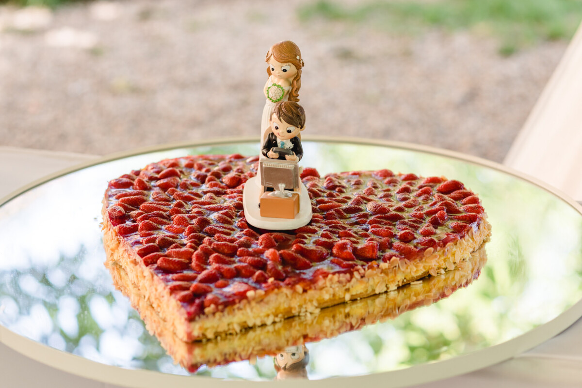 Herzförmiger Kuchen mit Erdbeerbelag und einer Braut- und Bräutigamfigur oben drauf.