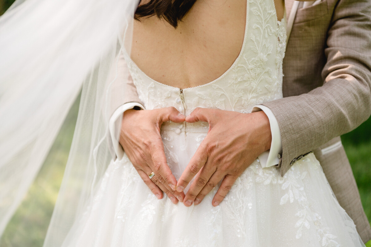 Ein Paar in Abendgarderobe bildet mit den Händen auf dem Rücken der Braut ein Herz.