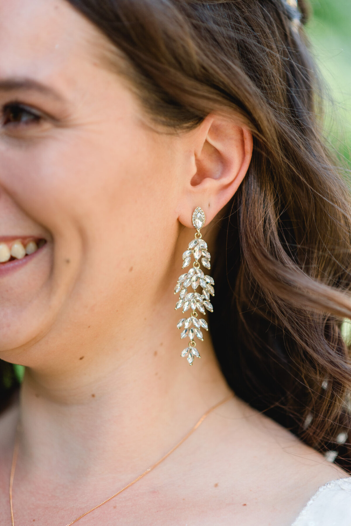 Nahaufnahme einer Frau, die einen langen, verzierten, blattförmigen Ohrring mit funkelnden Steinen trägt. Ihr Haar ist wellig und ihre Lippen sind zu einem sanften Lächeln geformt.