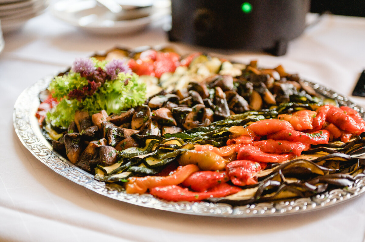 Eine Platte mit verschiedenen gegrillten Gemüsesorten, darunter Zucchini, Paprika, Pilze und Auberginen, garniert mit Salat und Kräutern.