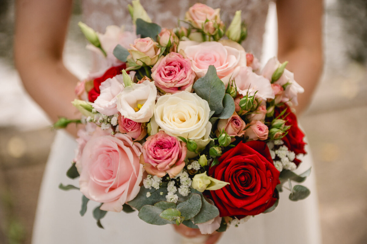 Eine Person hält einen Strauß rosa, roter und weißer Rosen gemischt mit Grün.