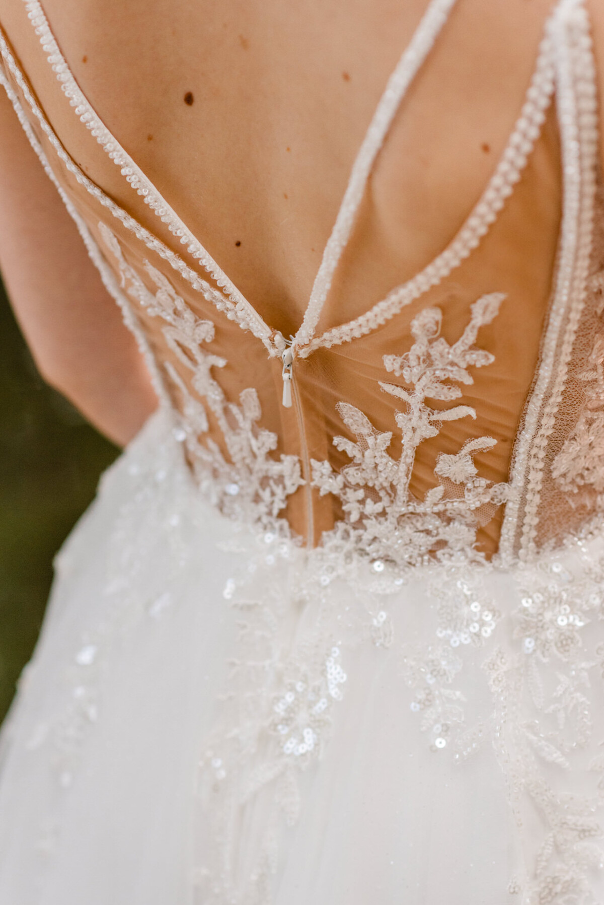 Nahaufnahme der Rückseite eines Brautkleides mit aufwendiger Spitze und Perlendetails und einem Reißverschluss.