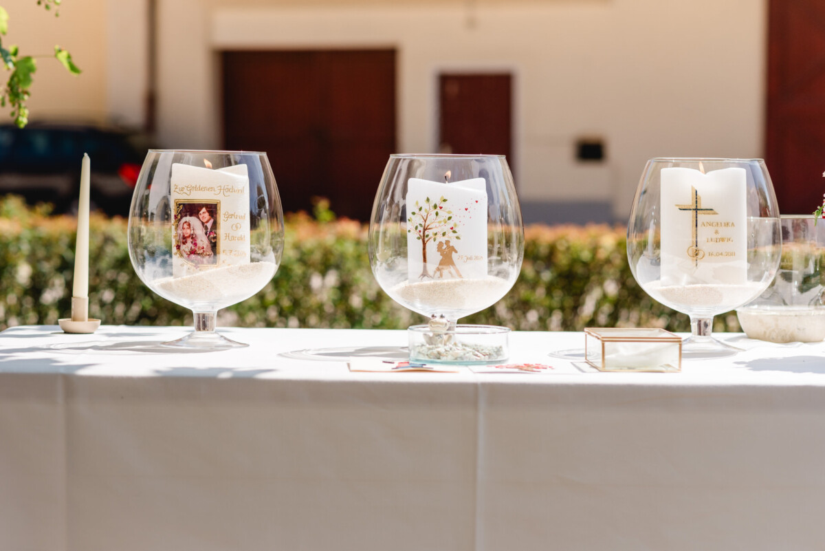 Drei dekorative Glasschalen auf einem Tisch halten Kerzen mit persönlichen Designs und Botschaften vor einem unscharfen Außenhintergrund.