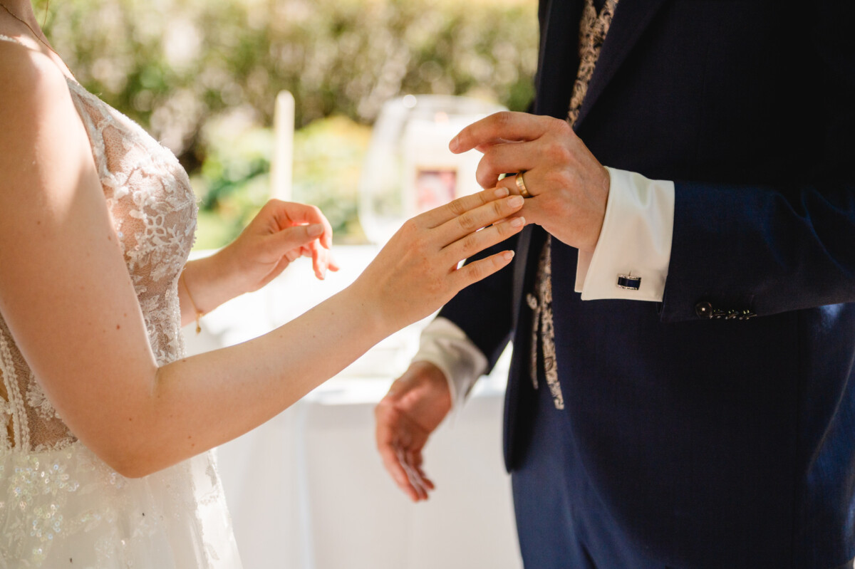 Ein Paar tauscht im Freien Eheringe aus, wobei der Fokus auf ihren Händen liegt.