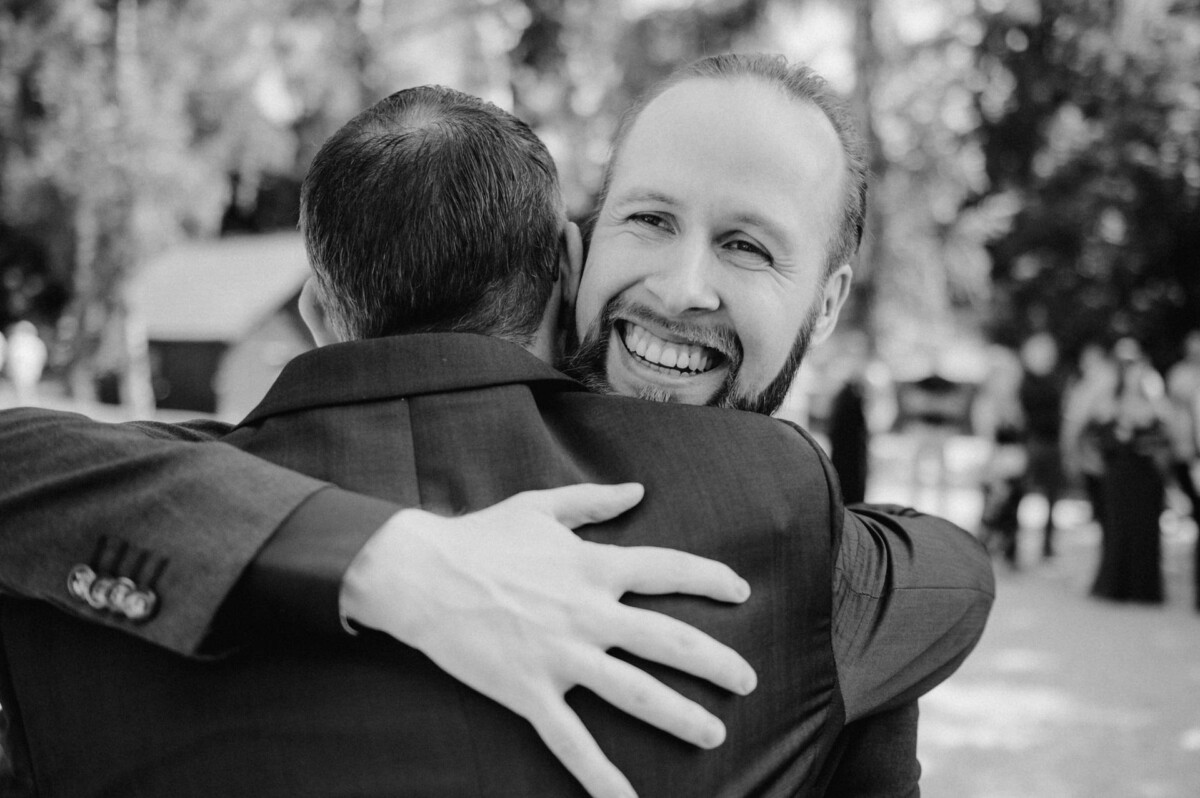 Zwei Männer umarmen sich herzlich im Freien; einer lächelt breit.