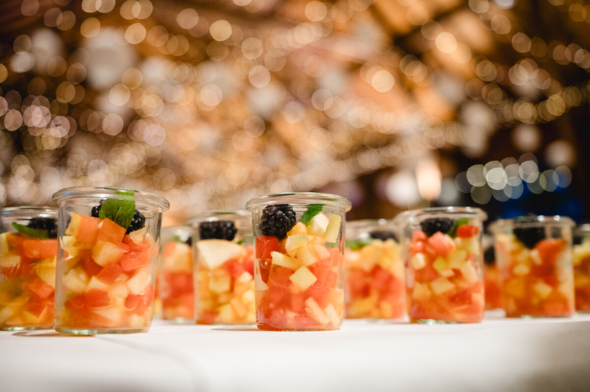 Gläser mit gewürfeltem Obst, garniert mit Brombeeren, auf einem Tisch mit verschwommenen dekorativen Lichtern im Hintergrund.
