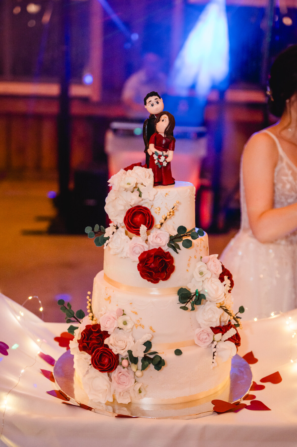 Eine dreistöckige Hochzeitstorte, dekoriert mit weißen und roten Blumen, gekrönt von der Figur eines Paares in Abendgarderobe.